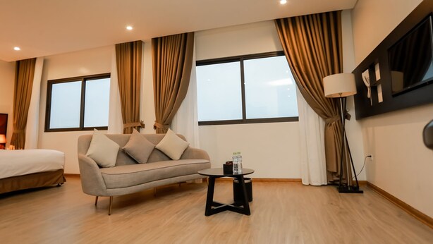 Quarto de hotel com sofá, uma pequena mesa, abajur e cama.