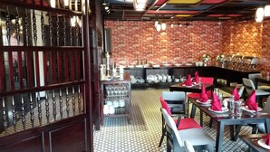 Um restaurante com paredes de tijolo, soalho estampado e mesas dispostas com guardanapos e pratos vermelhos.