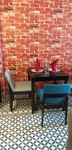 A dining area with a brick wall, patterned floor tiles, and two chairs with blue upholstery. - Max Boutique Hotel (Thuc Phan)