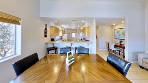 Uma sala de jantar moderna com uma mesa e cadeiras de madeira, uma cozinha ao fundo e um mapa na parede.
