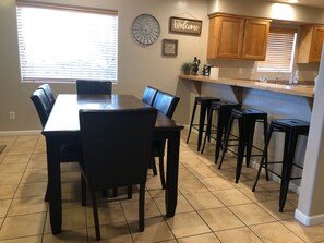 Un comedor con mesa y sillas de madera, una cocina con armarios de madera y un ventanal con persianas.