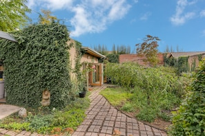 Stroll through the serene garden, lined with lush greenery and a variety of plants, to a traditional building with a brick facade.