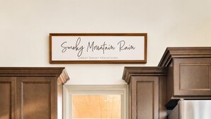 A kitchen with wooden cabinets, a stainless steel refrigerator, a window with a view of greenery, and a sign indicating a fire extinguisher inside. - Gatlinburg Cottage – Hot Tub, Walk Downtown (Gatlinburg)