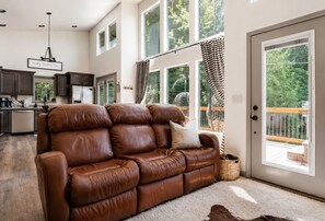 A spacious living area with a leather sofa, a kitchen in the background, and a large sliding glass door leading to an outdoor deck.