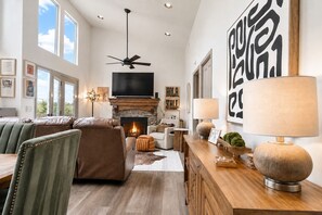 A spacious living room with a fireplace, a ceiling fan, and a large TV.