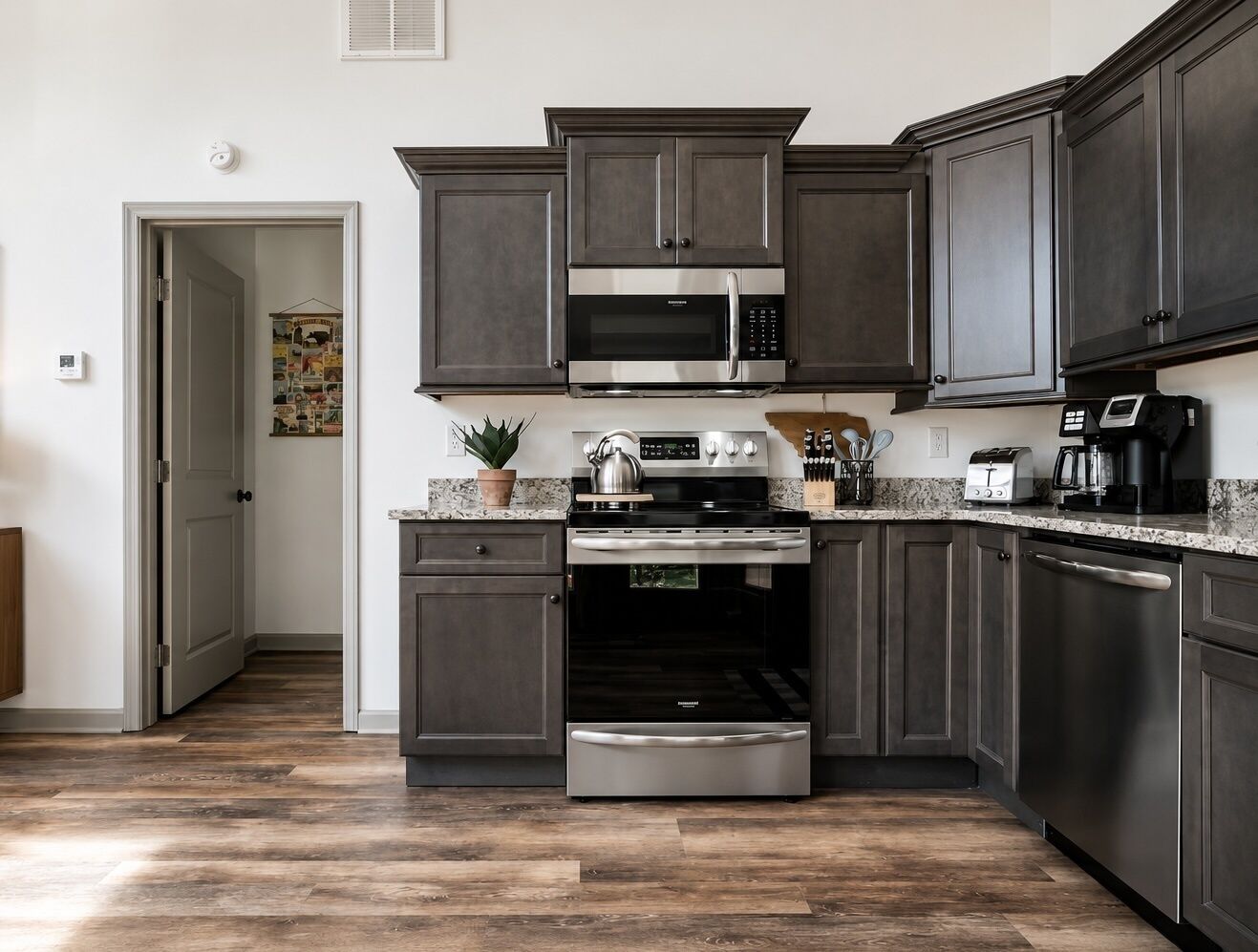 A kitchen with dark cabinetry, stainless steel appliances, a granite countertop, and a wooden floor.