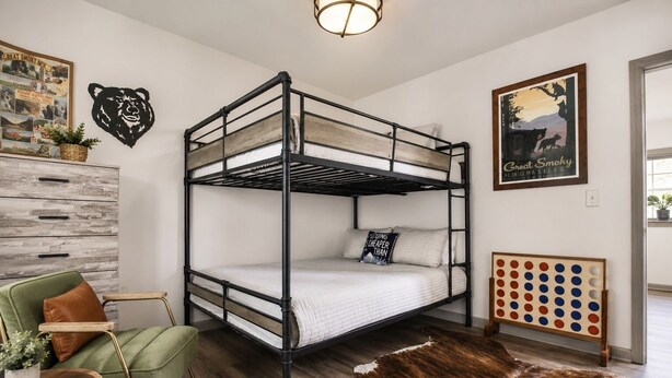 A bunk bed with a wooden frame, a green armchair, a small table with a plant, a cowhide rug, and wall art including a bear silhouette and a Great Smoky Mountains sign. - Gatlinburg Cottage – Hot Tub, Walk Downtown (Gatlinburg)
