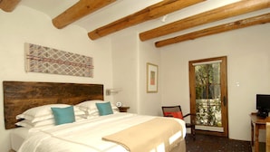 Um quarto com cabeceira de madeira, cama com roupa de cama branca e azul-turquesa, janela com vista para o verde e uma mesinha com uma televisão.