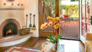 Uma sala de estar aconchegante com lareira, uma orquídea em vaso e vista para um pátio.
