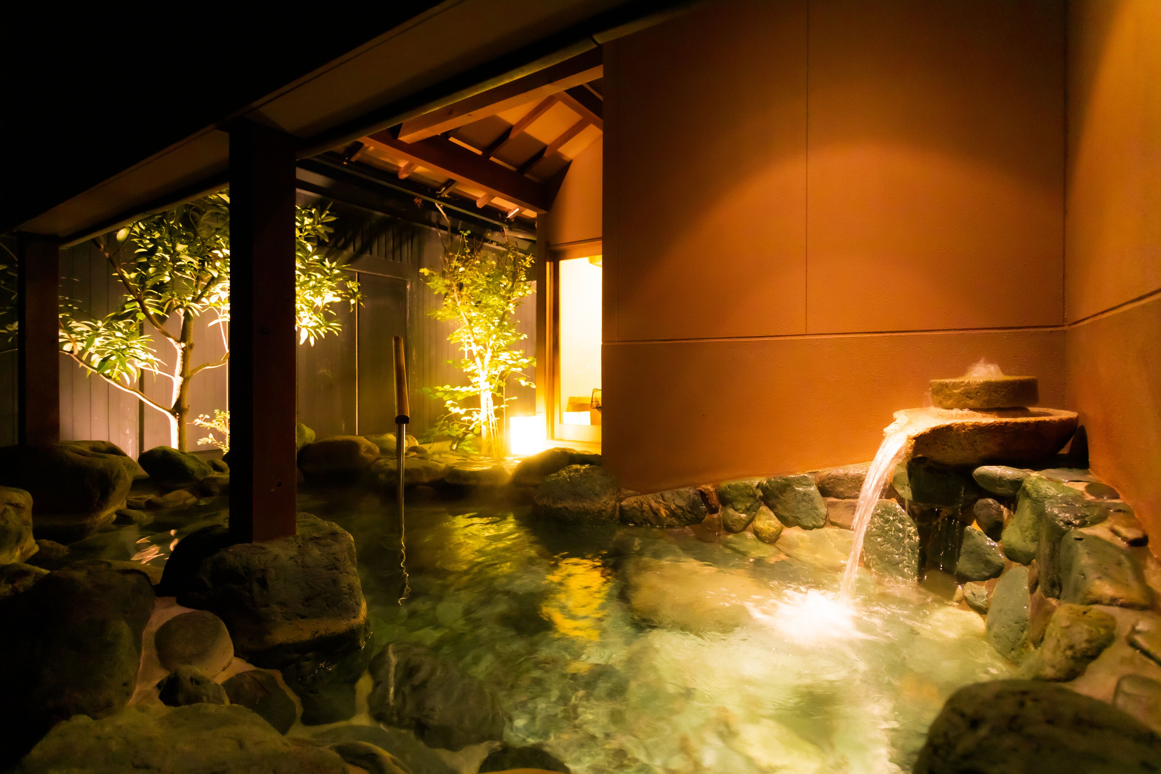 Un onsen japonés tradicional con un baño de piedra rodeado de rocas y una pequeña cascada.