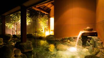 Un onsen japonés tradicional con un baño de piedra rodeado de rocas y una pequeña cascada.
