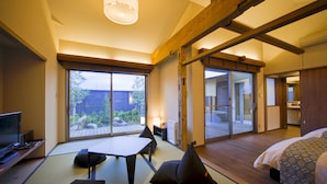 A traditional Japanese-style room with tatami flooring, a low table with cushions, a bed with patterned bedding, and large sliding doors leading to an outdoor area. - Migiwaya (Yaizu)
