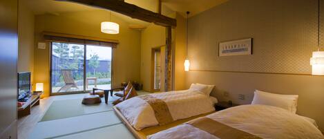 A hotel room with two beds, tatami mats, a television, and a sliding door leading to an outdoor area.