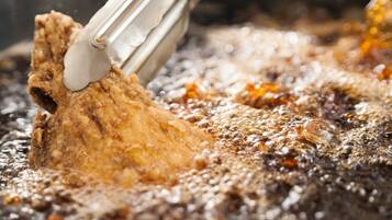Primer plano de un alimento frito que se levanta del aceite caliente.
