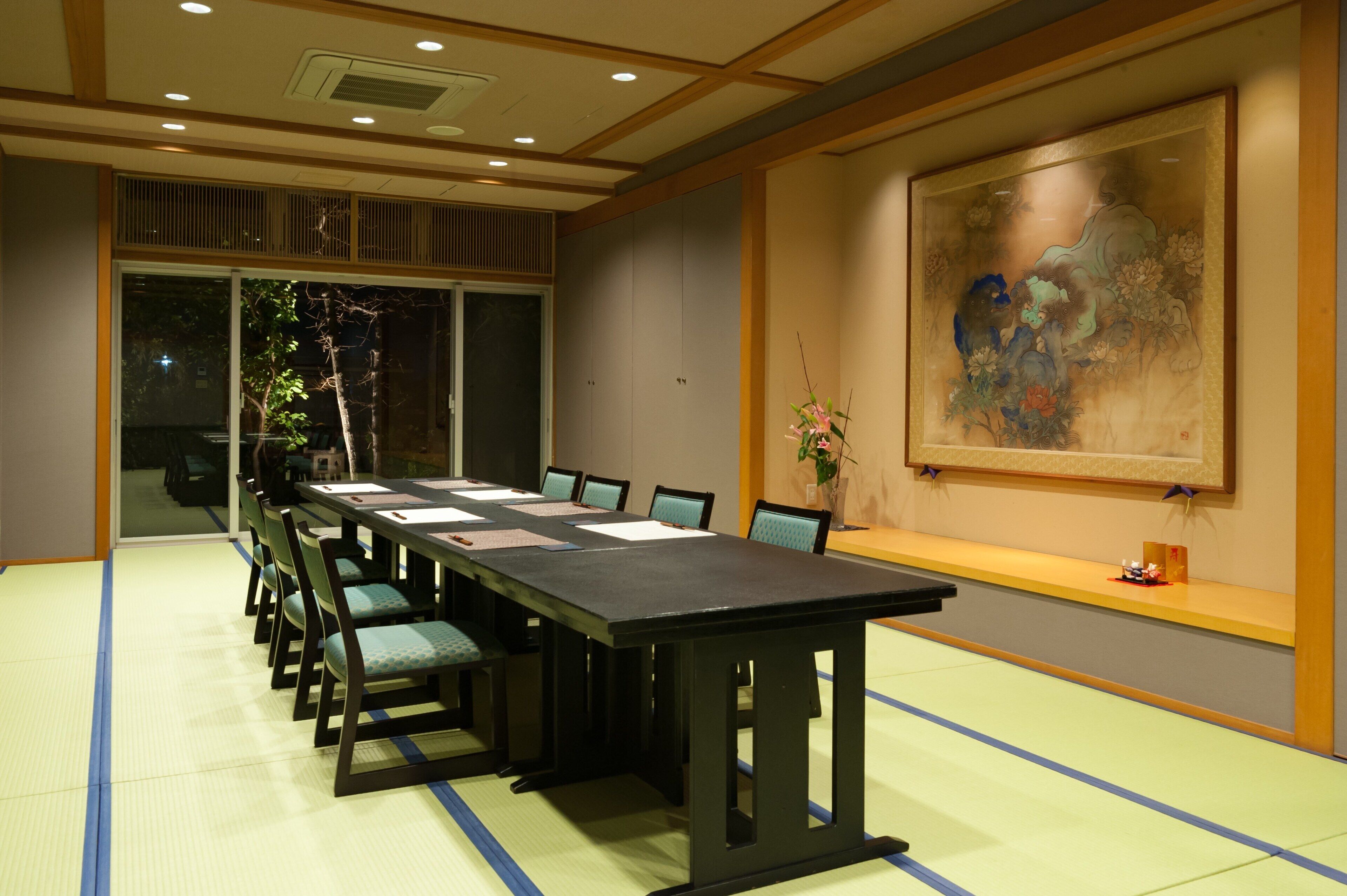 A conference room with a long table, chairs, a large painting, and a window.