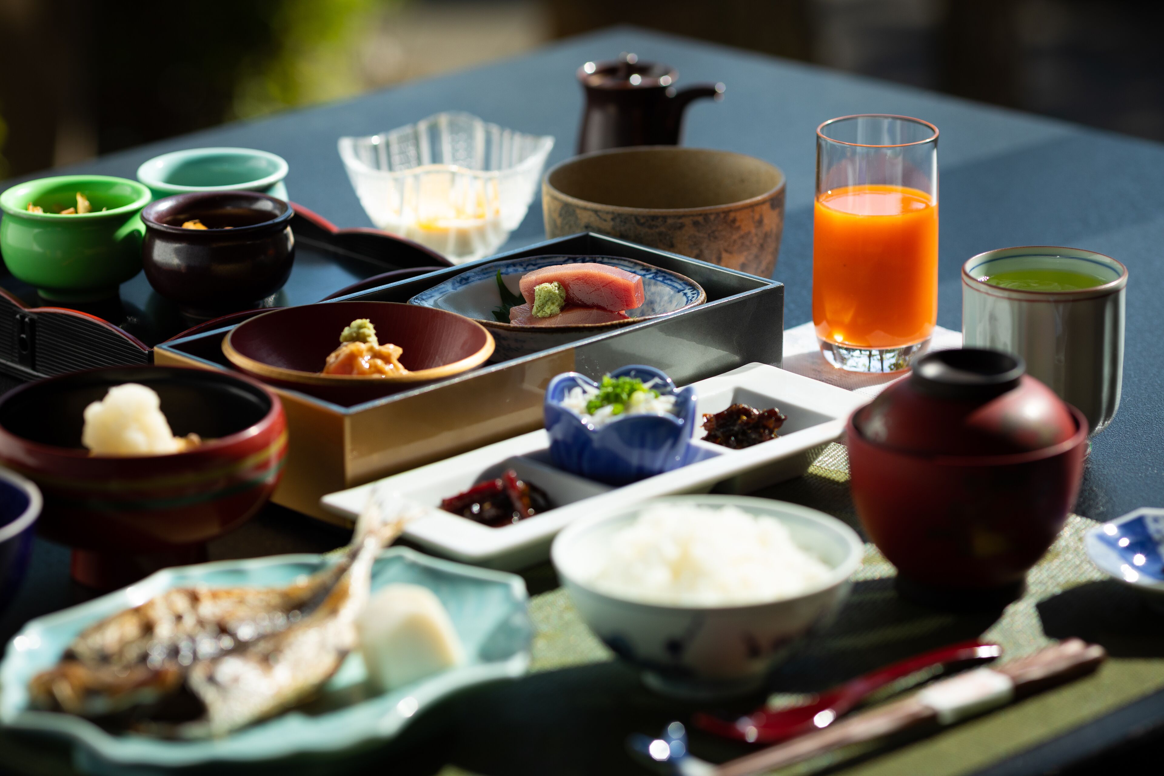 A variety of dishes and drinks on a table, including sushi, rice, and a glass of orange juice.