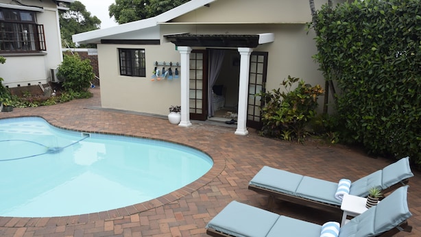 A swimming pool with lounge chairs, a covered patio, and a small garden area. - Berkeley House (Durban North)