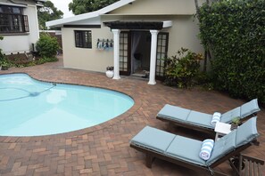A swimming pool with lounge chairs, a covered patio, and a small garden area. - Berkeley House (Durban North)