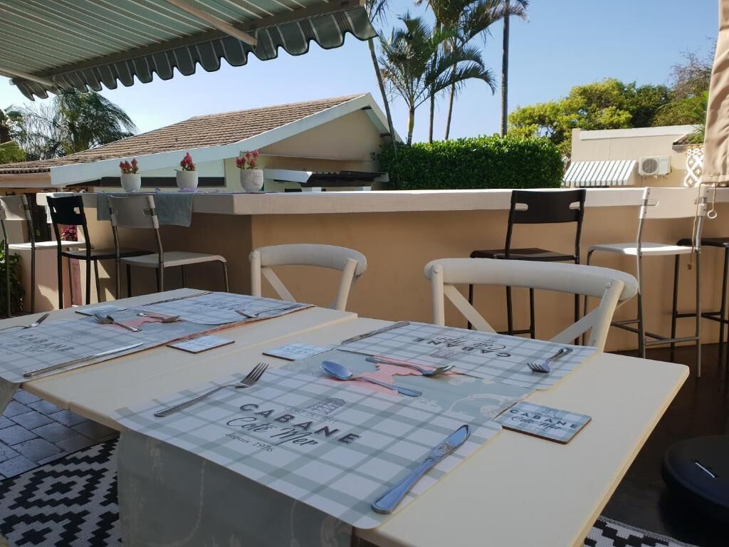 An outdoor dining area with tables set for two, featuring a checkered tablecloth and a menu titled "Café BANE."