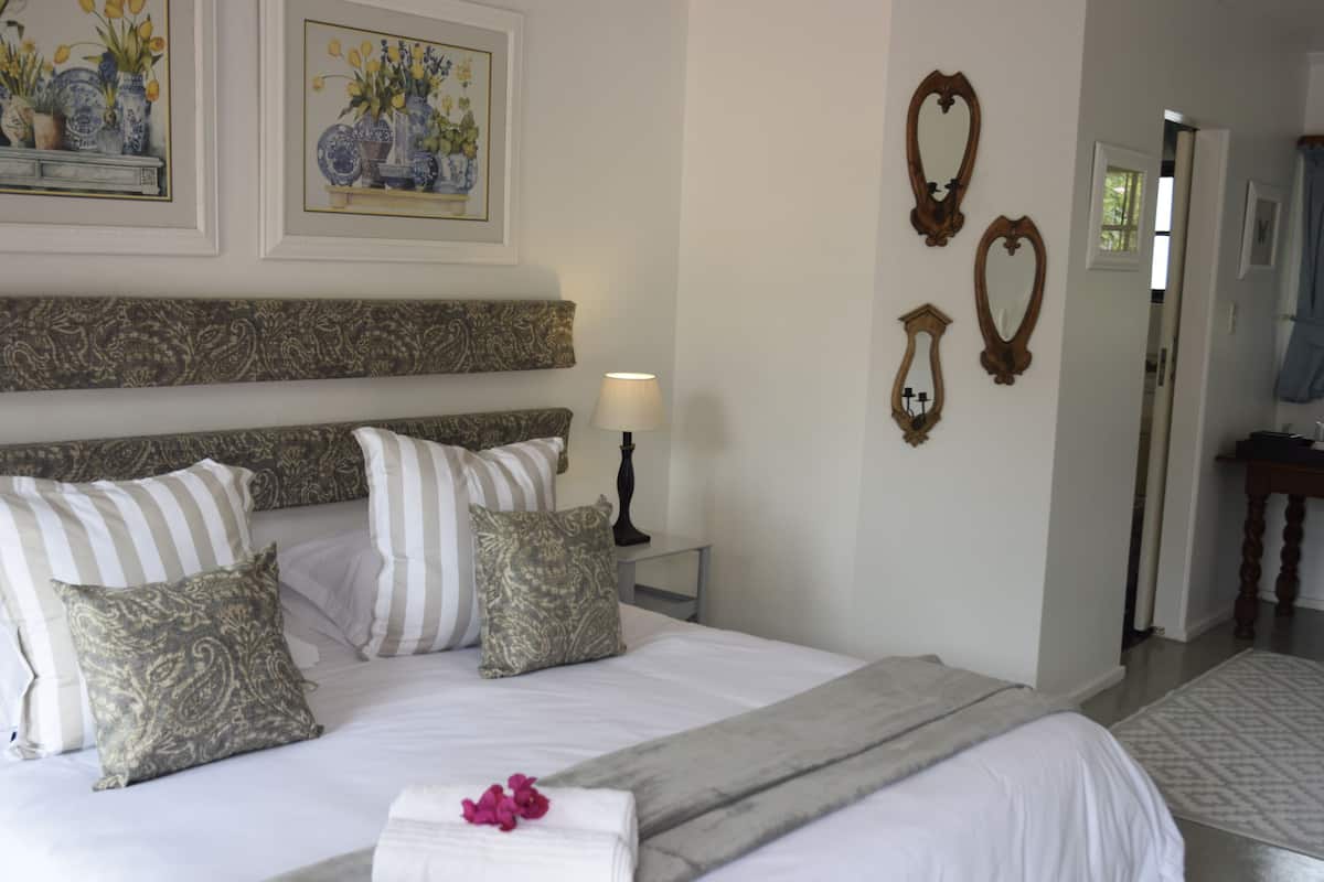 A neatly arranged bedroom with a large bed, decorative pillows, a bedside table with a lamp, and wall-mounted mirrors.