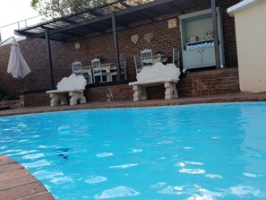 A swimming pool with stone benches and a covered patio area. - Berkeley House (Durban North)