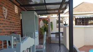A covered outdoor area with a wooden deck, a brick wall, and a small pool. - Berkeley House (Durban North)