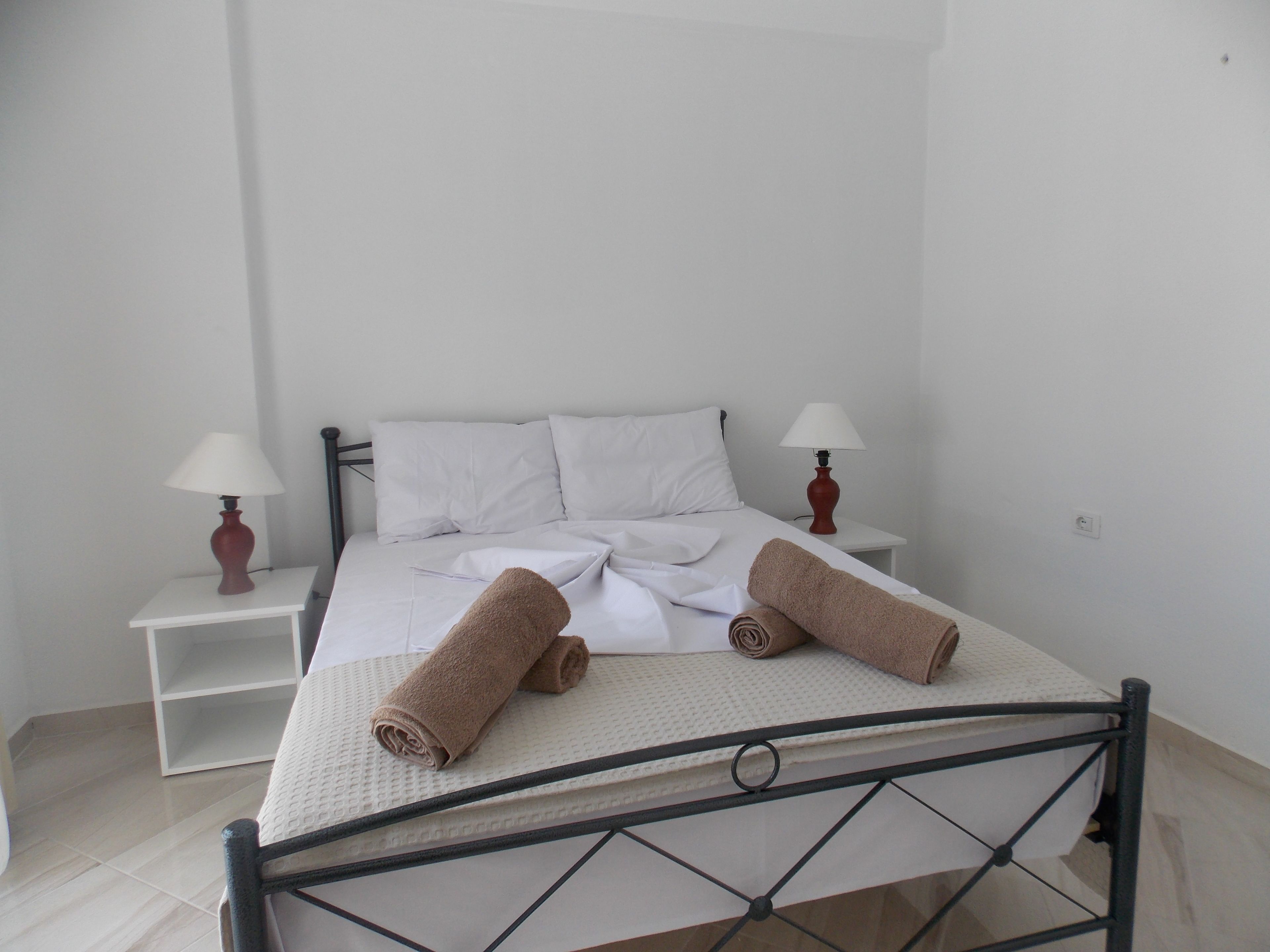 A neatly made bed with two rolled towels, two bedside lamps, and a white nightstand.