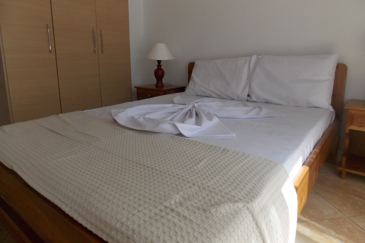A neatly made bed with a white duvet and a white pillow, a wooden wardrobe, and a bedside table with a lamp.