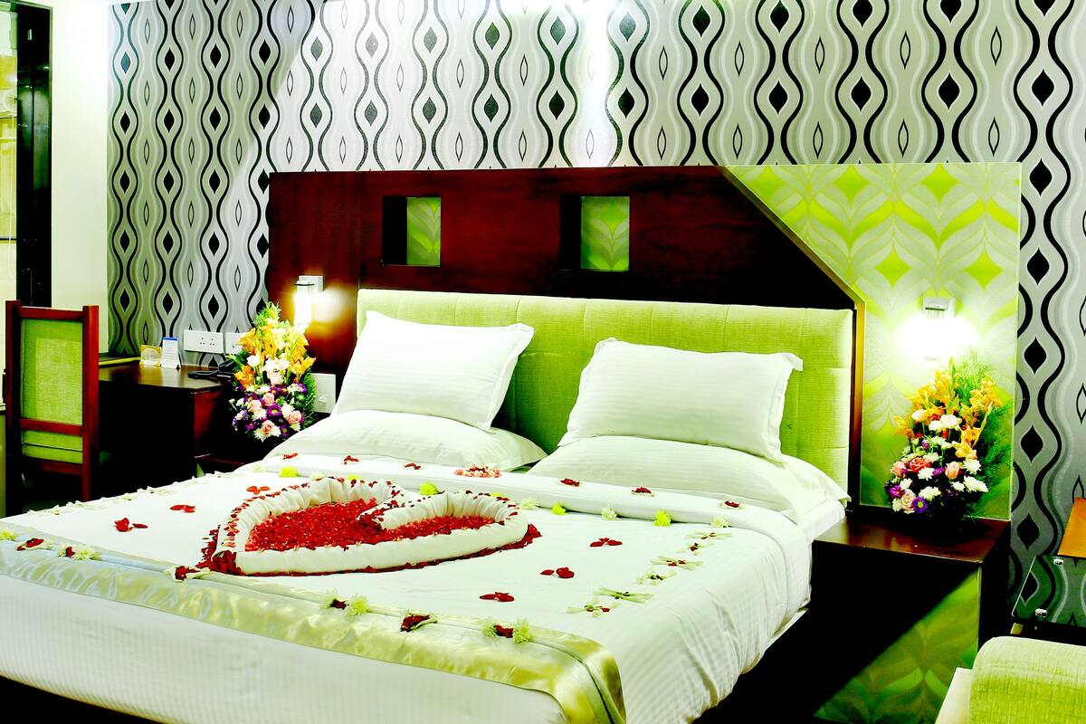 A hotel room with a large bed, a nightstand, a mirror, and a window.
