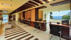 A modern hotel lobby with a long reception desk, multiple seating areas, and a view of the outdoors. - Gokulam Park Munnar (Devikolam)