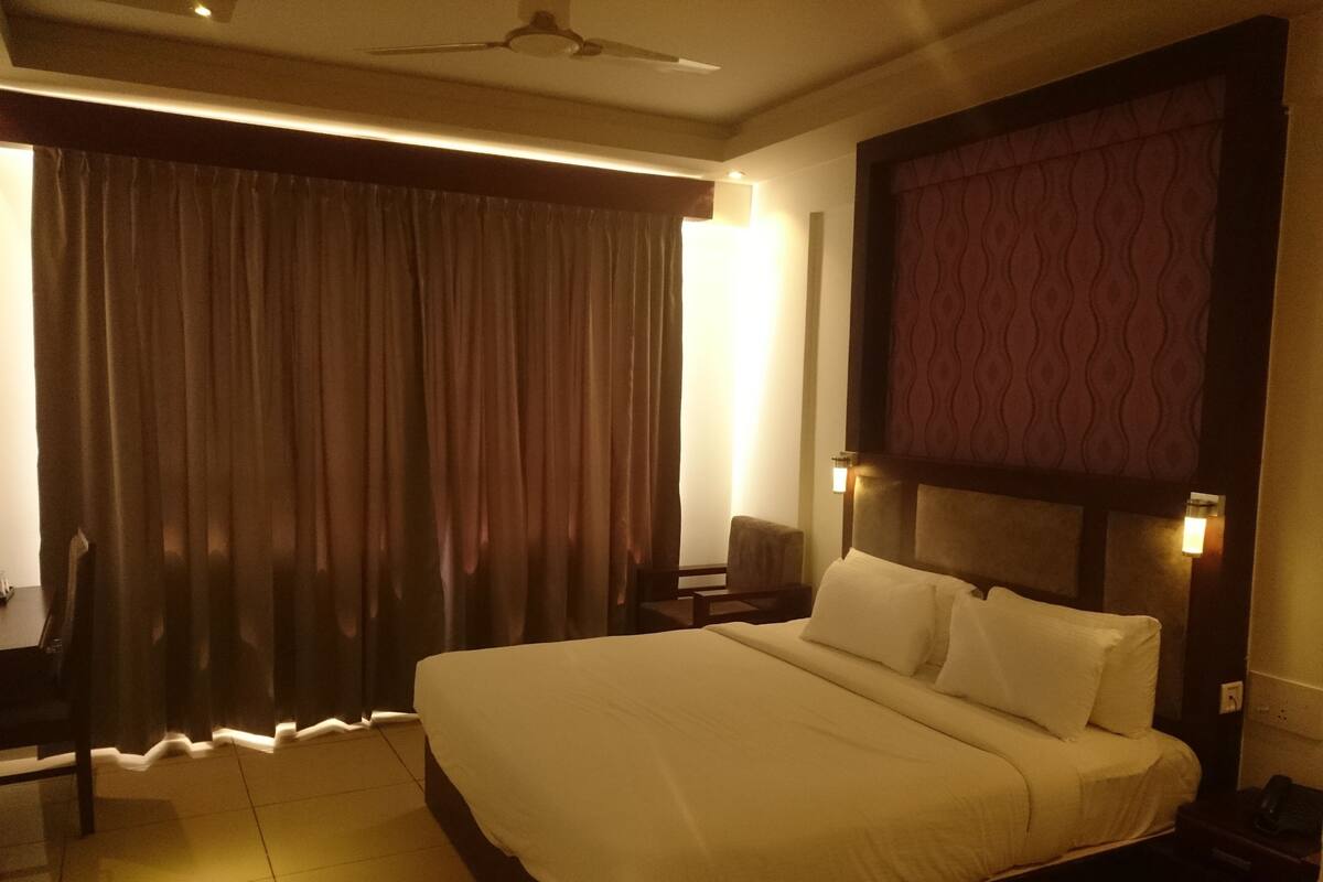 A hotel room with a large bed, a desk, a chair, a ceiling fan, and a window with curtains.