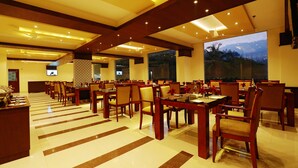 A spacious dining area with multiple tables and chairs, large windows with a view, and a ceiling with recessed lighting. - Gokulam Park Munnar (Devikolam)