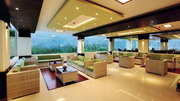A spacious lobby with multiple seating areas, large windows offering views of greenery, and a modern ceiling design. - Gokulam Park Munnar (Devikolam)