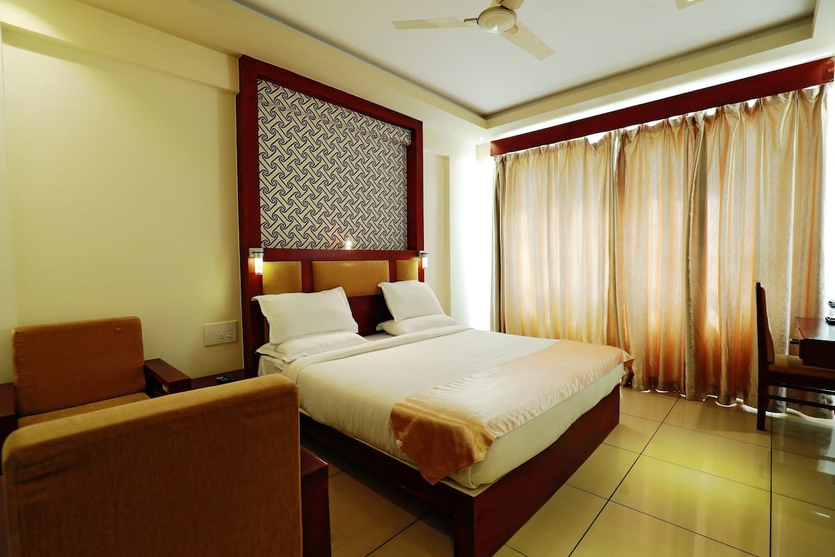 A hotel room with a bed, a chair, a desk, a ceiling fan, and a window with curtains.