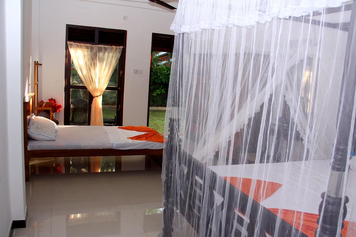 A room with a bed, a window with a sheer curtain, and a view of greenery outside.