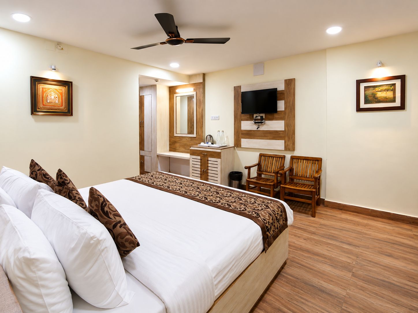 Ein Hotelzimmer mit Bett, Schreibtisch, Sessel, Fernseher und Deckenventilator.