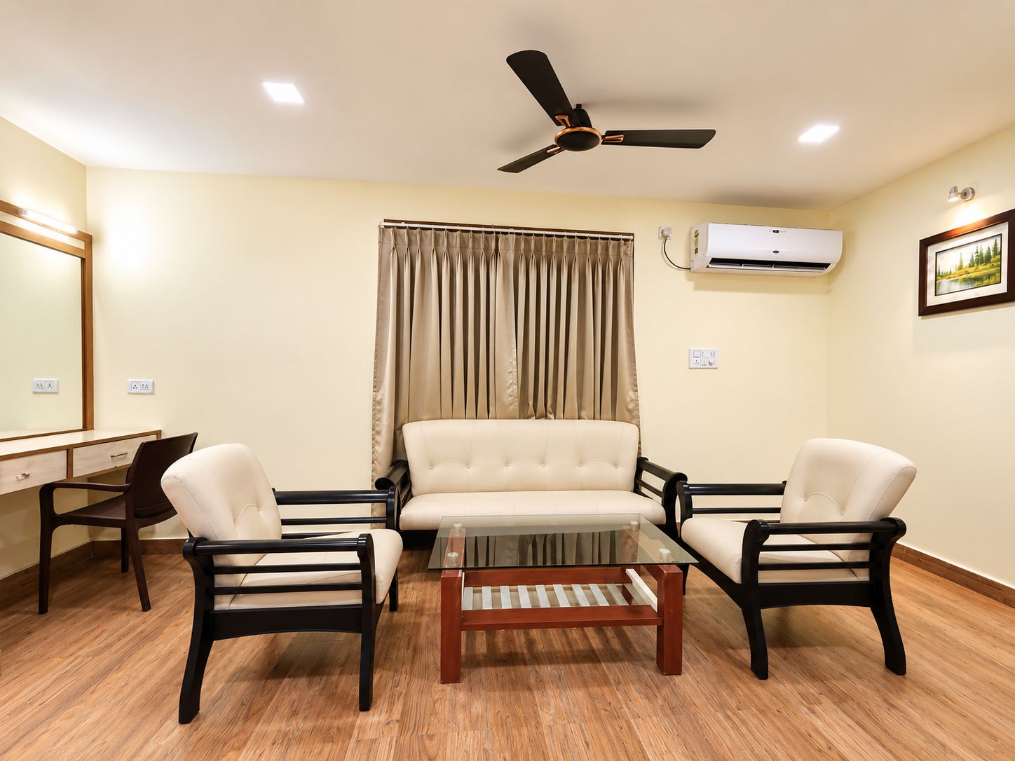 Una habitación con ventilador de techo, aire acondicionado, un escritorio con silla, sofá y mesa de centro.