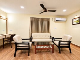 A room with a ceiling fan, an air conditioning unit, a desk with a chair, a sofa, and a coffee table.