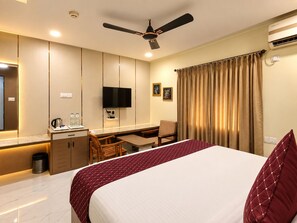 Habitación de hotel con cama, escritorio, silla y ventilador de techo.