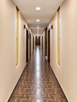 Un largo y estrecho pasillo de hotel con puertas a ambos lados, suelo de madera con diseño y luces empotradas en el techo.