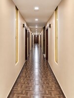 Un largo y estrecho pasillo de hotel con puertas a ambos lados, suelo de madera con diseño y luces empotradas en el techo.
