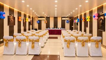 Ein Konferenzraum mit Reihen weißer Stühle mit goldenen Bändern, einem langen Tisch mit roter Tischdecke und bunten Ballons an den Wänden.