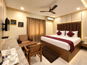 A hotel room with a bed, a desk, a chair, a television, and an air conditioning unit. - Hotel Arya Palace (Bhubaneshwar)