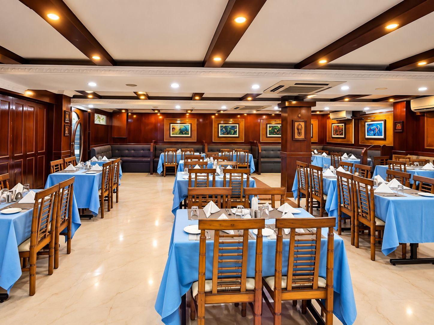 A restaurant with multiple tables and booths, wooden chairs, and blue tablecloths.