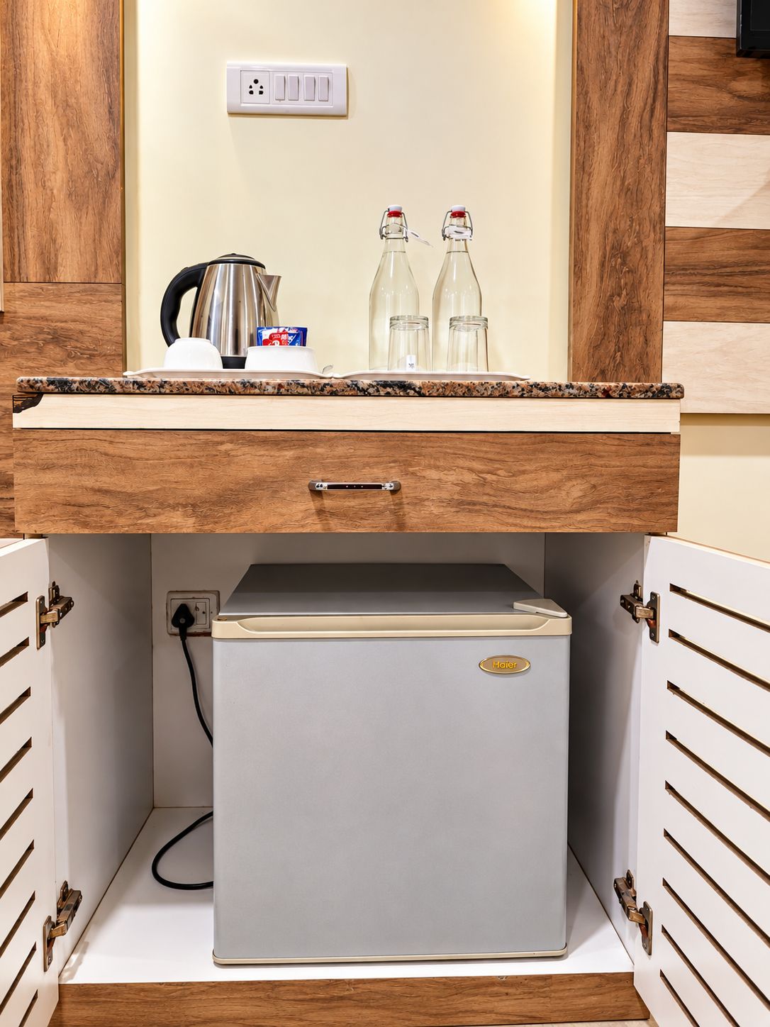 Una piccola cucina componibile con frigorifero integrato, macchina da caffè e due bottiglie sul piano di lavoro.