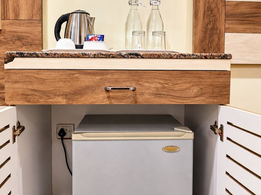Una piccola cucina componibile con frigorifero integrato, macchina da caffè e due bottiglie sul piano di lavoro.