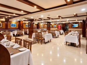 A restaurant with multiple tables and chairs, ceiling lights, and wall-mounted televisions. - Hotel Arya Palace (Bhubaneshwar)