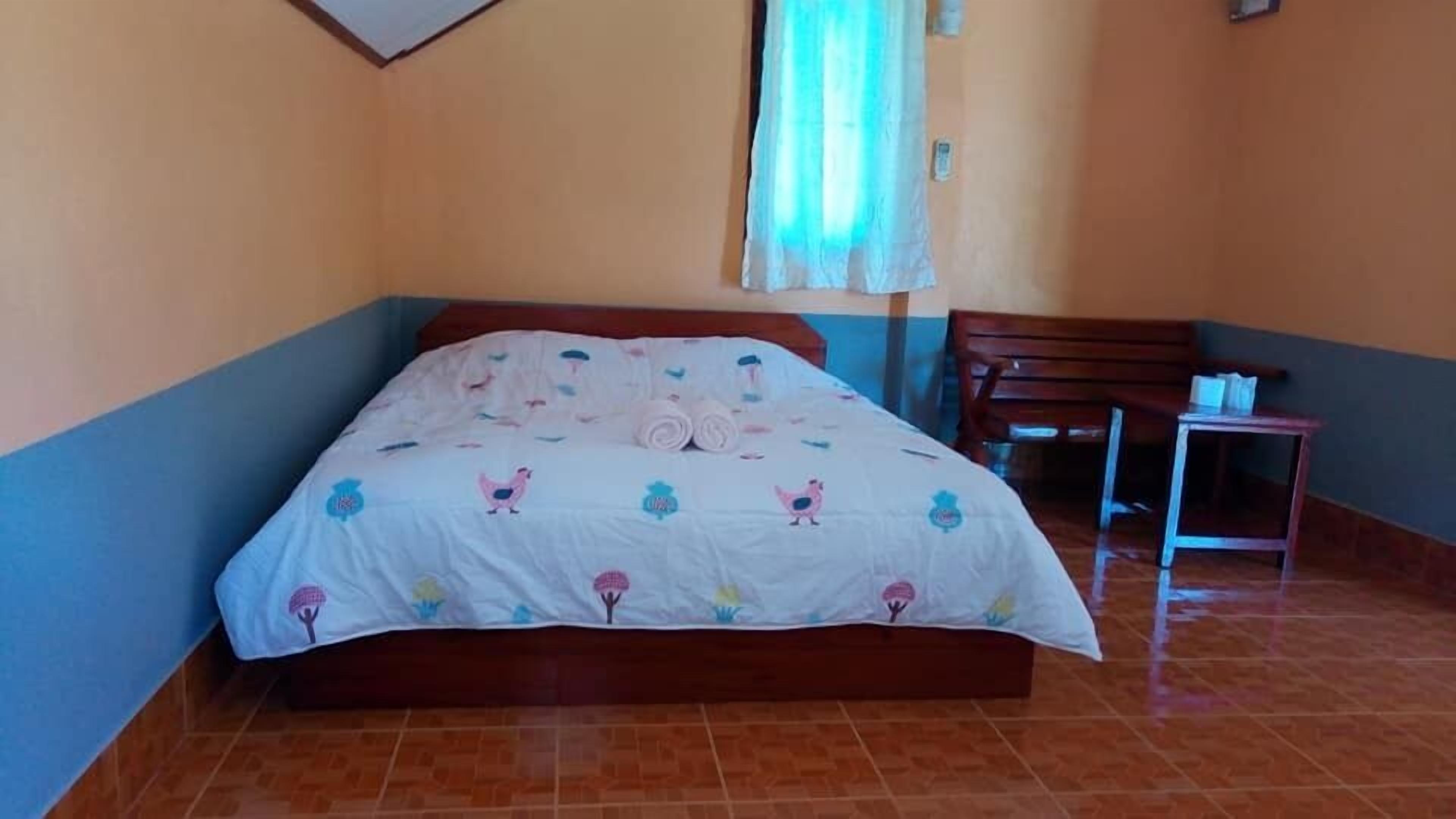 A bedroom with a bed, a chair, a small table, and a window with curtains.