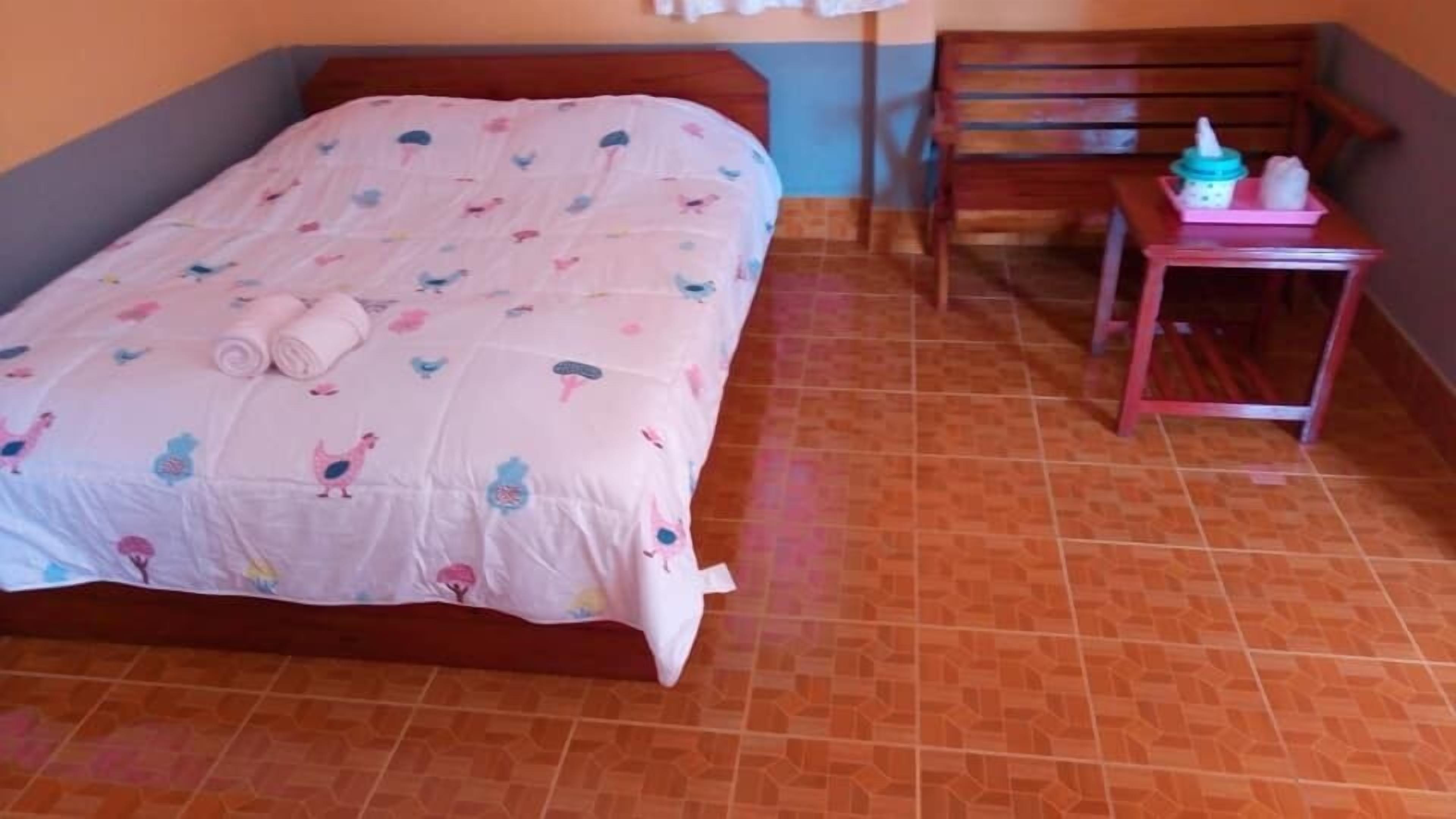 Un dormitorio con una cama, un banco de madera y una pequeña mesa con una botella y una taza.