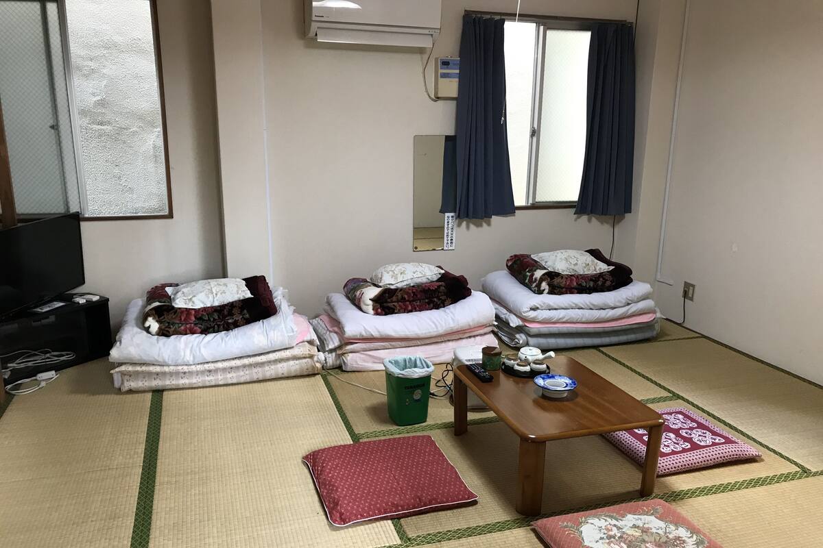 Een kamer met tatami matten, een televisie, een kachel en een futonbed met kussens.